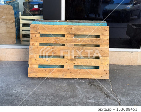 Wooden pallets stacked near storefront wall. Construction, recycling, and material reuse concept in urban industrial setting. 133088453