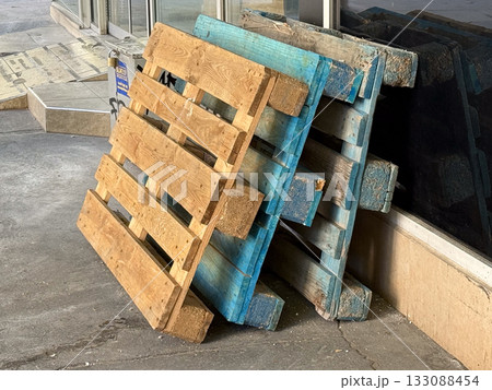 Wooden pallets stacked near storefront wall. Construction, recycling, and material reuse concept in urban industrial setting. 133088454