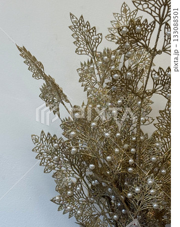 Golden decorative branch with pearl ornaments on wall background. Christmas decoration. Elegant home decor, festive arrangement, and holiday inspiration. Golden decorative branch with pearl ornaments on wall background. Christmas decoration. Elegant home decor, festive arrangement, and holiday inspiration. 133088501