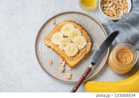 Peanut butter toast and banana in a plate on a light background with nuts Peanut butter toast and banana in a plate on a light background with nuts 133088834