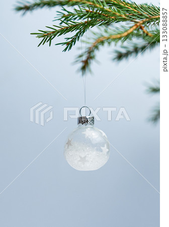 Fir branches with a ball-shaped Christmas tree ornament on a light blue background. 133088857
