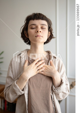 Portrait of inspired young woman with hands on chest for breath control, deep mindful meditation Portrait of inspired young woman with hands on chest for breath control, deep mindful meditation 133089087