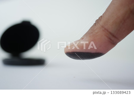 Finger with black ink near an open inkpad on a white surface Finger with black ink near an open inkpad on a white surface 133089423