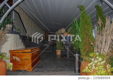 Long covered hallway with rustic decor and lush greenery. Indoor corridor with rustic decor features wooden floors and a wooden chest. 133089504