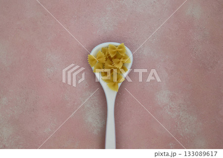 Raw pasta farfalle on wooden spoon on black background. Top view of Italian cuisine ingredient. 133089617