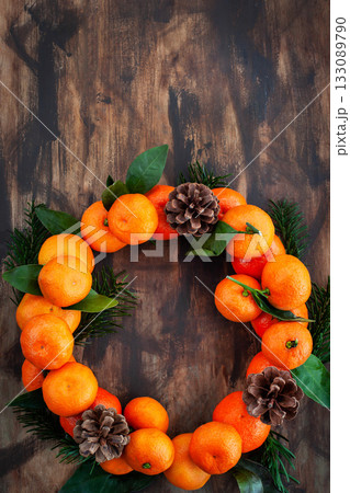 Wreath of fresh ripe tangerines with leaves and cones, on wooden background, top view 133089790