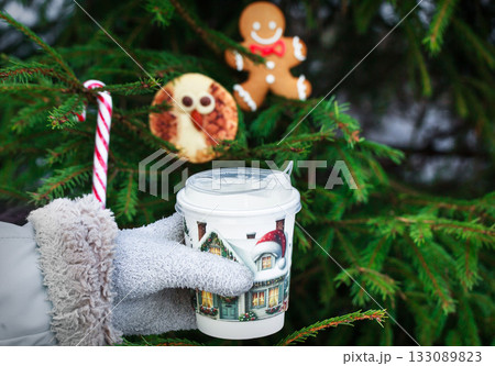 Woman`s hand hold a cup of coffee on Christmas cookies and fir-tree background, outdoor Woman`s hand hold a cup of coffee on Christmas cookies and fir-tree background, outdoor 133089823