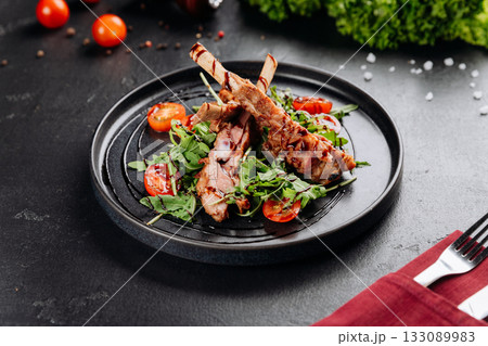 Grilled ribs on arugula with cherry tomatoes and balsamic glaze, restaurant plating 133089983