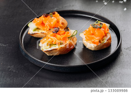 Gourmet salmon canapes on baguette with cream cheese and cucumber on black plate Gourmet salmon canapes on baguette with cream cheese and cucumber on black plate 133089986
