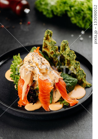 Smoked salmon salad with poached egg, hollandaise and spinach waffles on black plate Smoked salmon salad with poached egg, hollandaise and spinach waffles on black plate 133090012