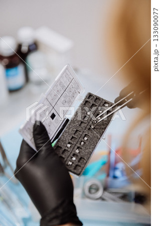 Orthodontic bracket kit with placement chart and tweezers, gloved hands, clinic closeup 133090077