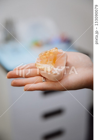 Transparent implant surgical guide on dental jaw model in clinician hand, clinic closeup 133090079