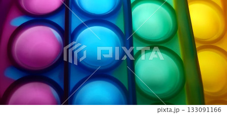 Vibrant rainbow pop it fidget toy close-up. Close-up of a multicolored pop it fidget toy, featuring rows of bubble-like protrusions in vibrant colors: red, orange, yellow, green, blue, and purple. 133091166
