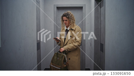 Female Guest Pauses in Hallway, Holding Luggage While Checking Smartphone. Female Guest Pauses in Hallway, Holding Luggage While Checking Smartphone. 133091650