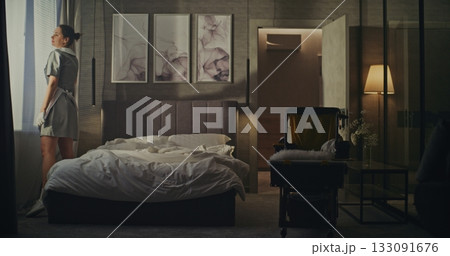 Woman in Neat Uniform Enters Room With Cleaning Trolley, Removes Used Bed Linens After Guest Checkout 133091676