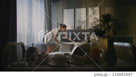 Attentive Female Housekeeper in Uniform Straightens Bedding and Open Curtains in Stylish Hotel Suite Attentive Female Housekeeper in Uniform Straightens Bedding and Open Curtains in Stylish Hotel Suite 133091697