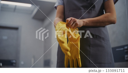 Careful Preparation on Cleaning. Hotel Housekeeper in Uniform Puts on Bright Yellow Cleaning Gloves 133091711