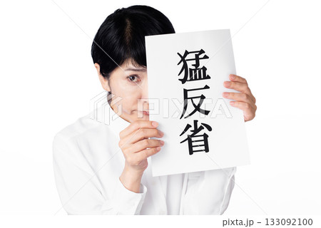 猛反省と書かれた紙を持ち恐る恐る視線を送るシニア女性 133092100