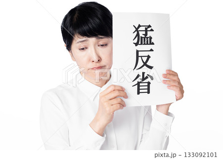 猛反省と書かれた紙を持ち視線を落とす白いシャツを着たシニア女性 猛反省と書かれた紙を持ち視線を落とす白いシャツを着たシニア女性 133092101