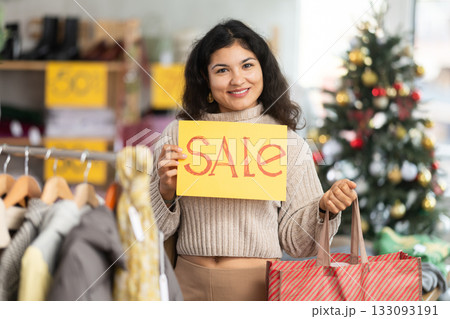 Latina woman standing in a store at a Christmas sale with a yellow poster Latina woman standing in a store at a Christmas sale with a yellow poster 133093191