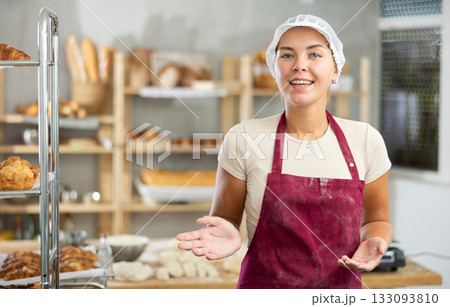 Young baker girl is standing near work table in kitchen, working with dough Young baker girl is standing near work table in kitchen, working with dough 133093810