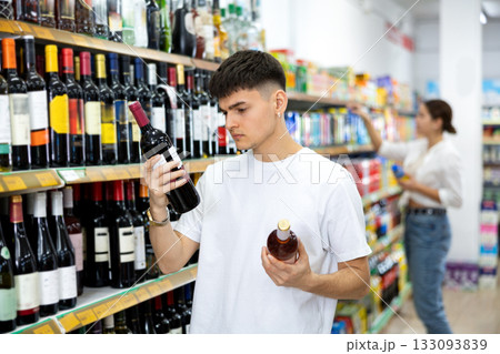 in supermarket young man carefully chooses wine 133093839