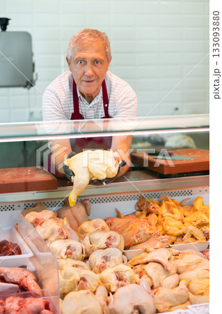 In butcher shop, senior man salesperson in gloves shows damp fresh poultry In butcher shop, senior man salesperson in gloves shows damp fresh poultry 133093880
