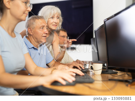 Old man learning computer programs with teacher in training room Old man learning computer programs with teacher in training room 133093881