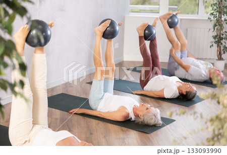 Active women doing pilates with soft ball lying on back in gym 133093990