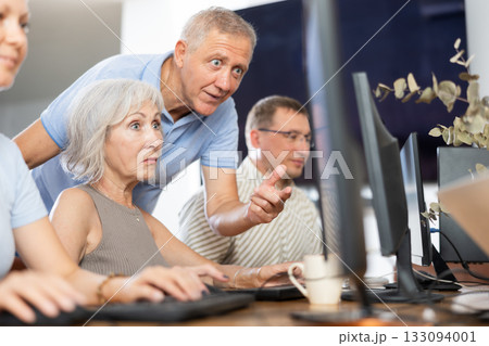 Older mentor explaining something to elderly woman during computer class 133094001