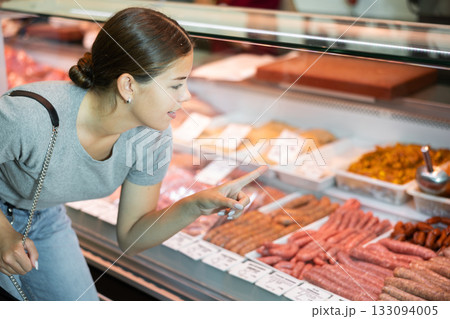 Female girl customer points with finger and orders chorizo meat snacks 133094005