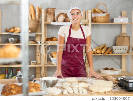 Smiling young female baker pausing during kneading dough in bakery Smiling young female baker pausing during kneading dough in bakery 133094007