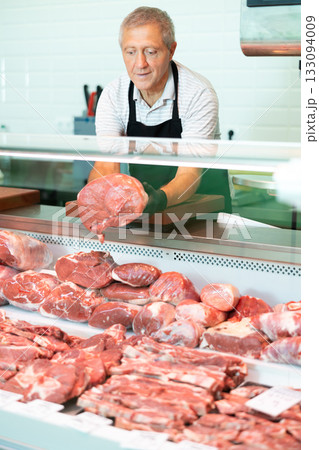 Male farmer of meat products in butcher shop offers to buy fresh beef tenderloin. 133094009