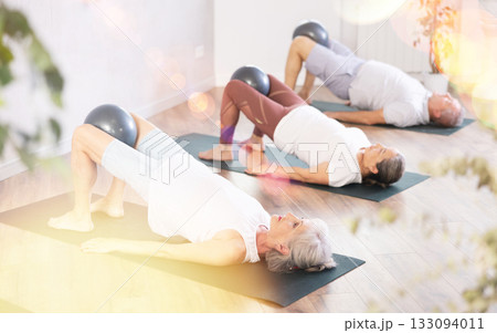 Lady does lightweight bridge pose - Setu Bandhasana and holds softball in lap. 133094011