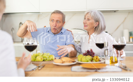 Mature married couple with female friend are sitting at table, enjoying food and wine, chatting. Mature married couple with female friend are sitting at table, enjoying food and wine, chatting. 133094012