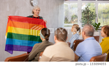 Focused adult students sitting at lesson with classmates, listening mature teacher talking about LGBT community and showing rainbow flag 133094055