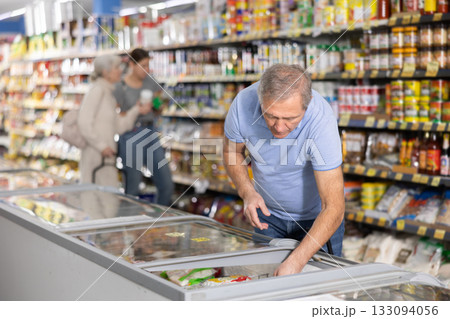 Mature man shopping in supermarket, choosing frozen convenience food Mature man shopping in supermarket, choosing frozen convenience food 133094056