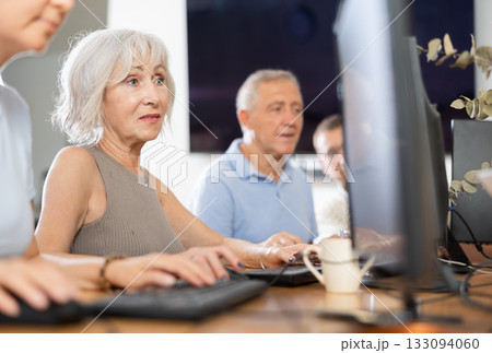 Portrait of an elderly positive woman working on computer with group of friends while attending PC classes in nursing home 133094060