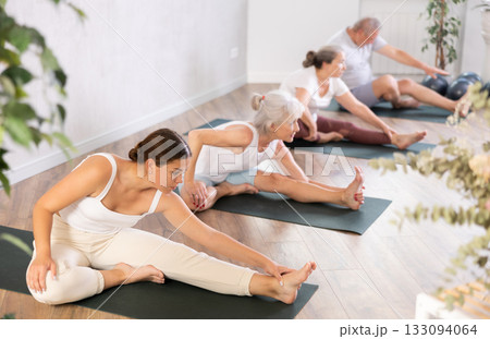 Mature positive women doing body stretching in yoga class Mature positive women doing body stretching in yoga class 133094064