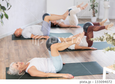 People lying on karemat, pulled bent legs to themselves and clamped soft-ball in knee People lying on karemat, pulled bent legs to themselves and clamped soft-ball in knee 133094072