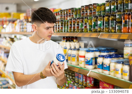Young male customer diligently picking out jar of mayonnaise Young male customer diligently picking out jar of mayonnaise 133094078