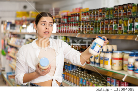 Young female customer diligently picking out jar of mayonnaise Young female customer diligently picking out jar of mayonnaise 133094089