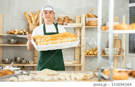 Young male baker holding baguettes in wicker basket 133094164