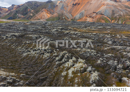 Rugged volcanic lava fields with moss patches in the foreground and colorful rhyolite mountains in the Landmannalaugar region of Iceland. 133094721