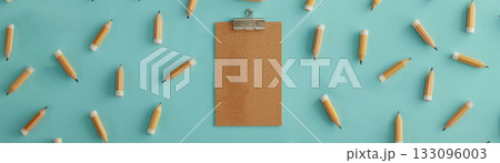 A clipboard surrounded by pencils on a vibrant blue surface, ideal for educational or creative projects. 133096003