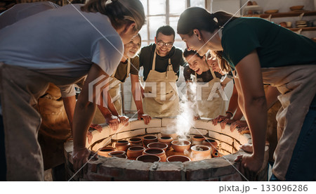 Excited group of artisans admiring the results of the pottery kiln firing process in a creative 133096286