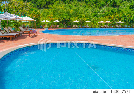 swimming pool at a tropical luxury resort by sea in summer. Tourism and recreation. Landscape with a pool and sun loungers and umbrellas swimming pool at a tropical luxury resort by sea in summer. Tourism and recreation. Landscape with a pool and sun loungers and umbrellas 133097571
