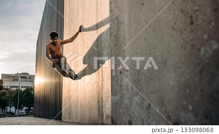 Dynamic parkour athlete defying gravity with amazing jump and shadow projection along a building Dynamic parkour athlete defying gravity with amazing jump and shadow projection along a building 133098068