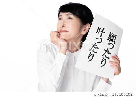 願ったり叶ったりと書かれた紙を持ち頬杖をつきながら笑顔を浮かべるシニア女性 願ったり叶ったりと書かれた紙を持ち頬杖をつきながら笑顔を浮かべるシニア女性 133100102