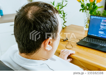 A man sits at a laptop and uses AI, seen from behind. 133102108